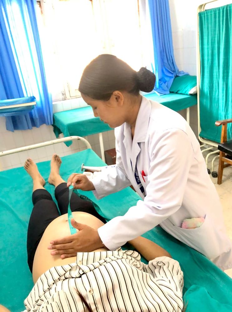 A midwifery student in a white coat examining a pregnant woman on a hospital ward
